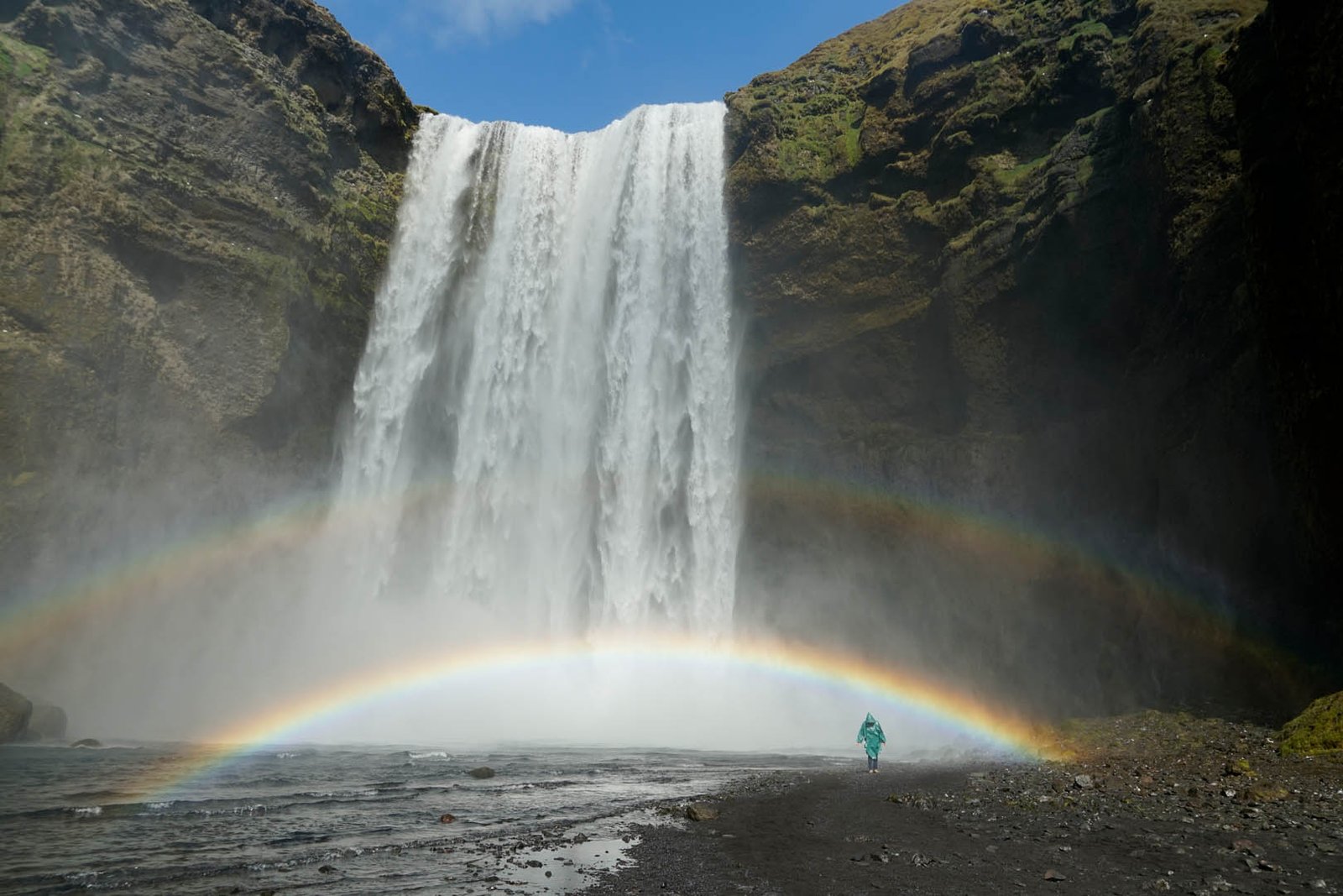 Skógafoss waterfall with a rainbow and a person walking in front